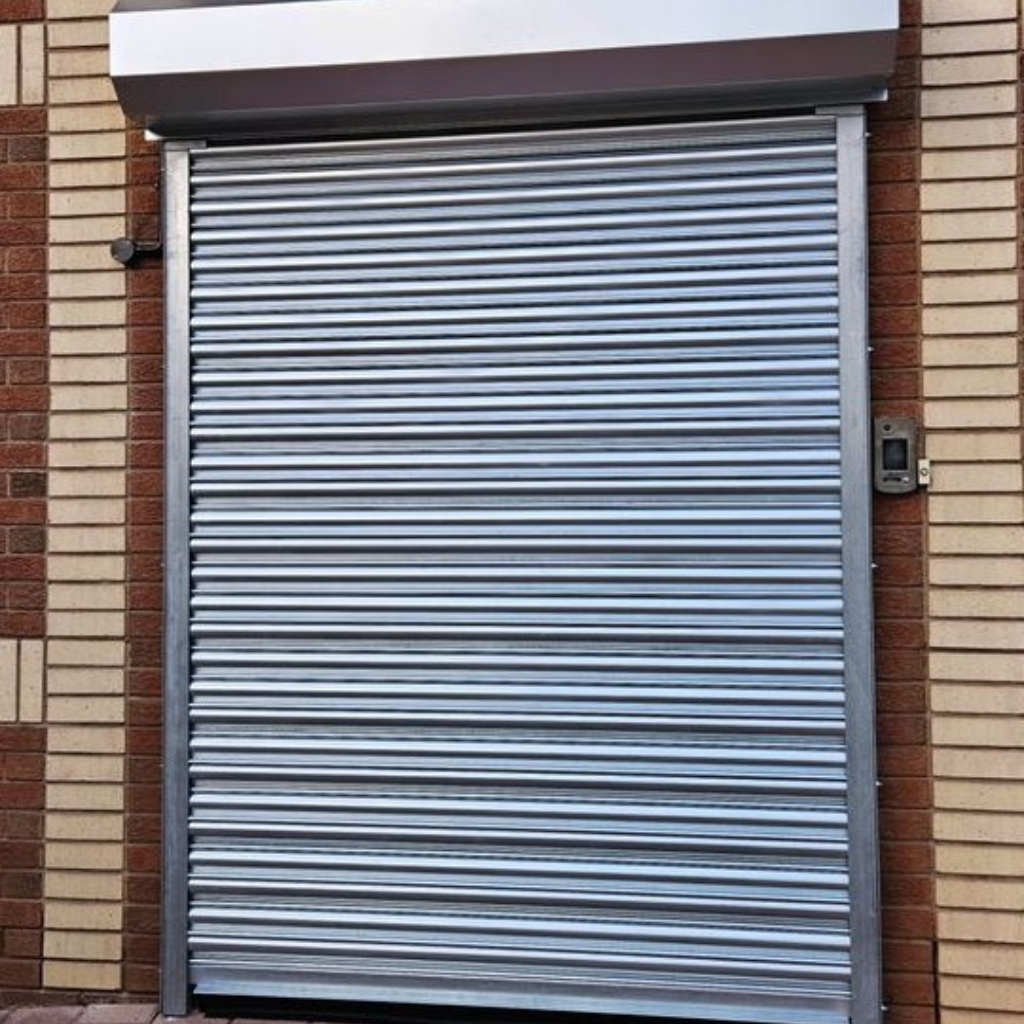A brown industrial rolling security gate installed on a commercial building storefront.
