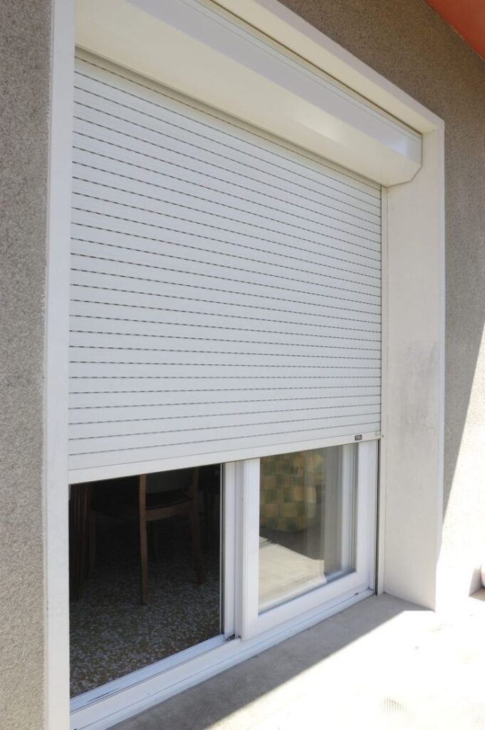 Exterior window with a white roller shutter, partially closed over a sliding glass door on a modern home facade.