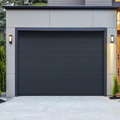 Modern home exterior with a dark gray garage door featuring horizontal ribbed panels, framed by light cladding and wall sconces above a concrete driveway.