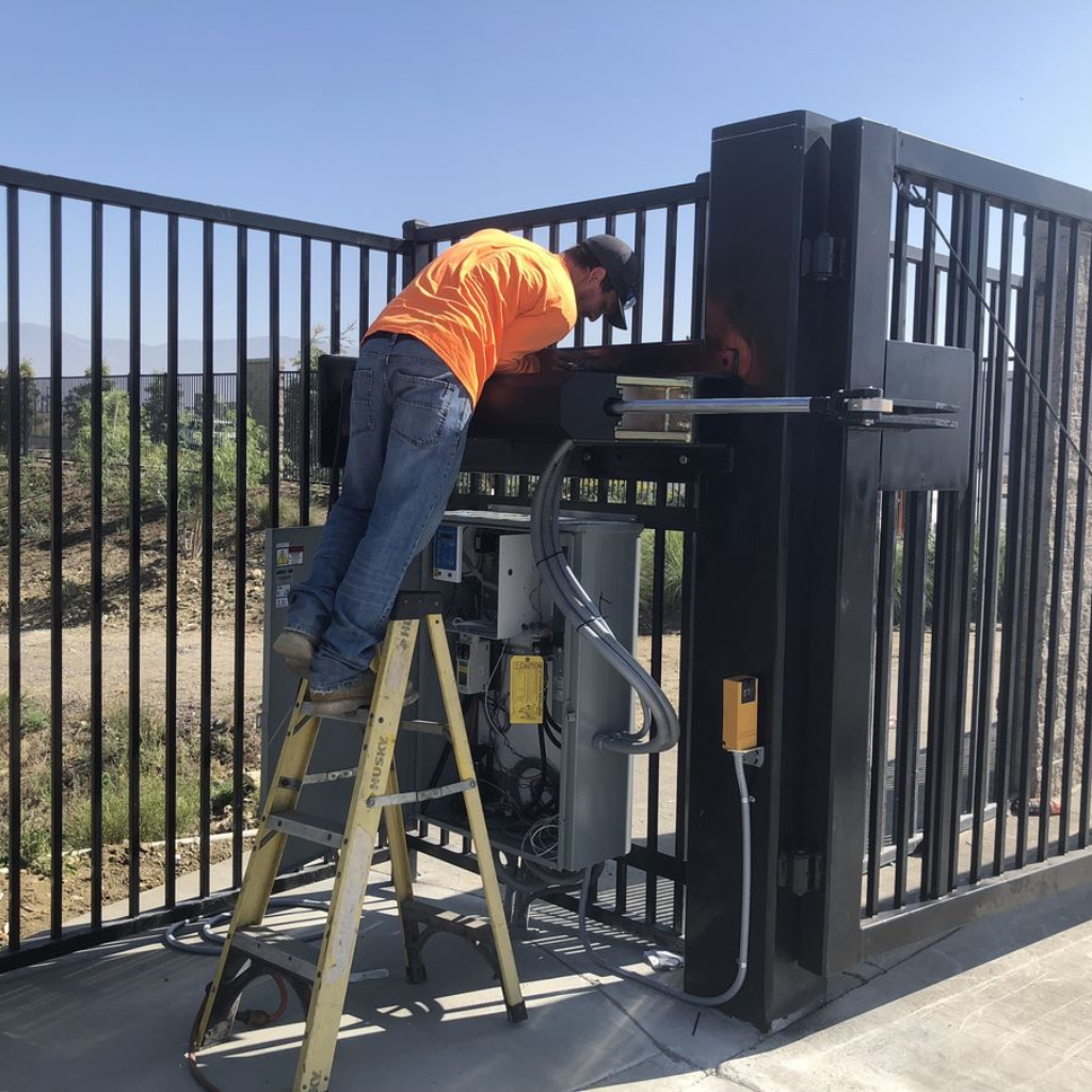 Technician installing automatic electric sliding gate motor on a black steel security gate.