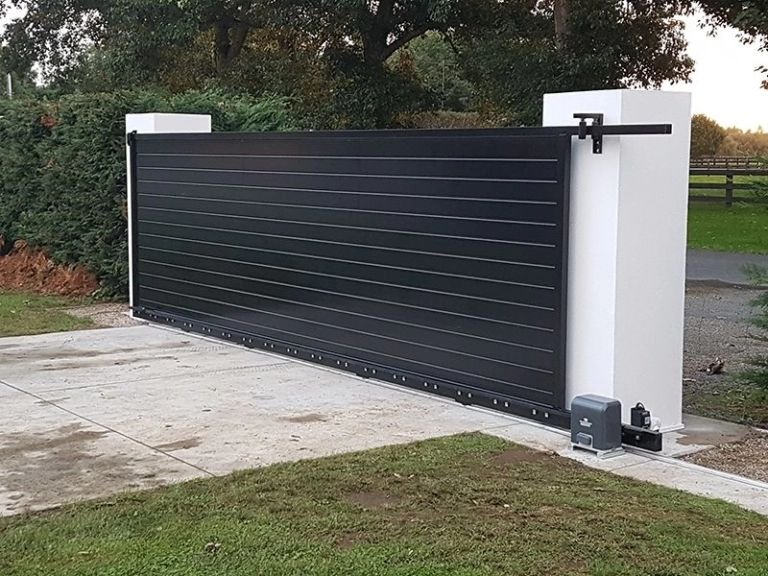 Black horizontal-panel sliding driveway gate with an automatic gate motor, installed between white masonry pillars at a residential entrance.